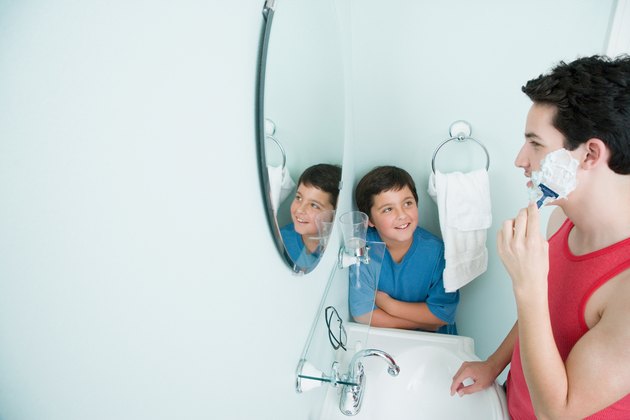 Boy watching brother shave in bathroom