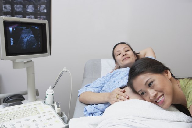 Asian woman listening to sister's pregnant belly in hospital