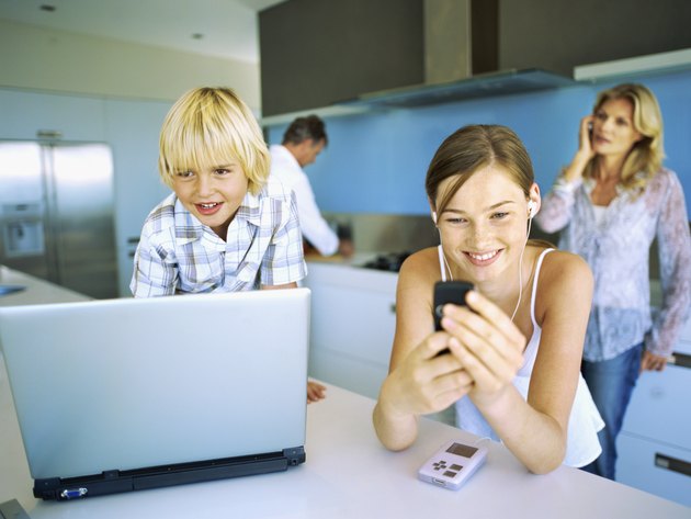 Close-up of two children in front of a laptop with their parents standing behind them