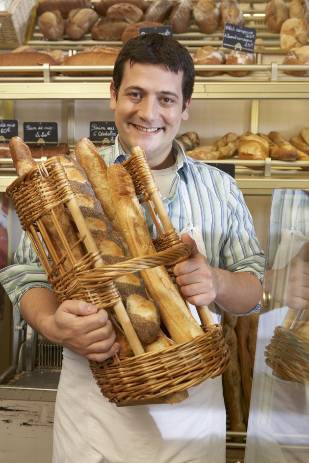 Young man in bakery, holding basket of baguettes, smiling, portrait