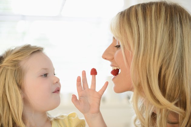 Girl feeding mother with raspberries from her fingers