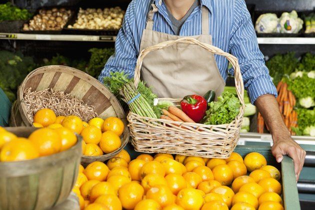 Midsection of man standing near oranges stall with vegetable basket in supermarket