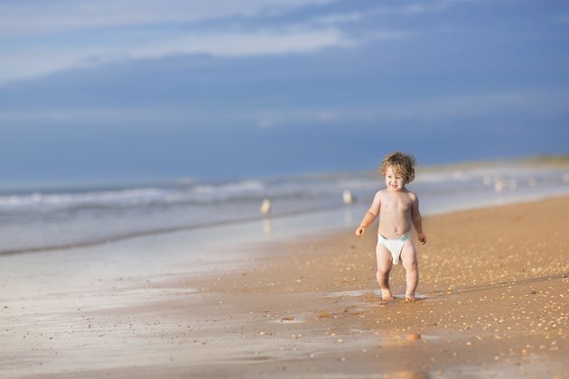 Cute baby girl with curly hair running on beautiful beach