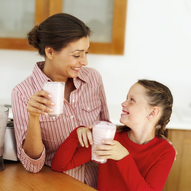 Young mother and a young girl (8-10) holding glasses of strawberry milk shakes looking at each other