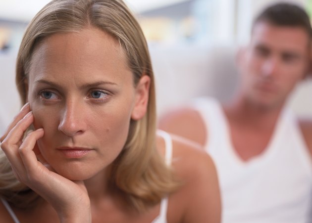 Young woman sitting resting her chin on her hand with a young man sitting behind