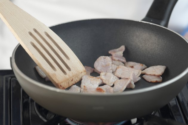 Stirring bacon in a frying pan, studio shot