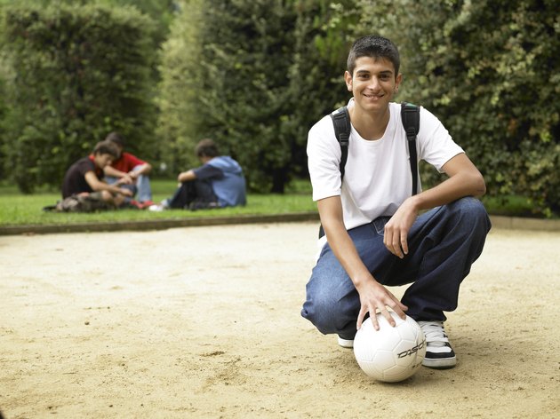 Teenage boy (15-17) kneeling with soccer ball at park