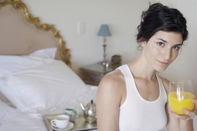 Young woman drinking orange juice on bed (portrait)
