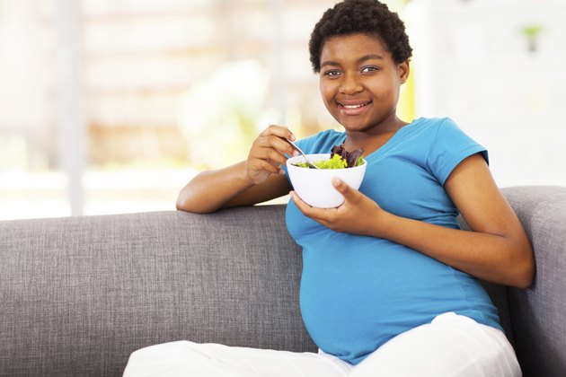 pregnant african woman eating green salad on sofa