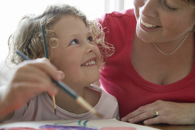 "Girl (3-5) painting picture, looking up at mother, smiling"