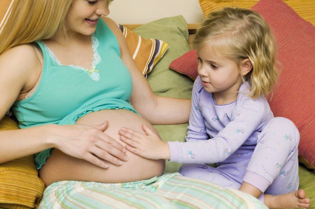 Girl (4-5) sitting on bed touching belly of pregnant mother, close-up