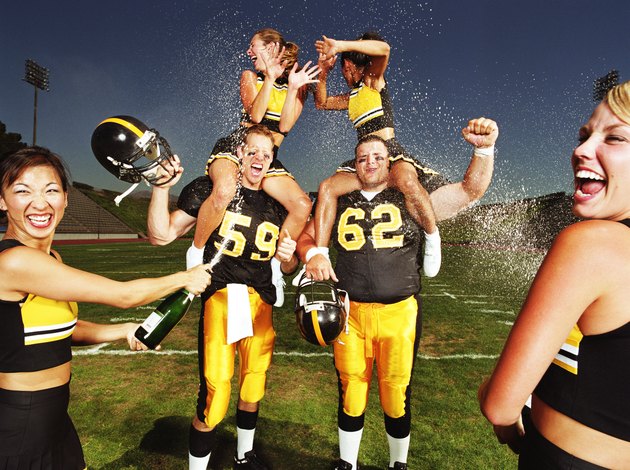 Two football players with cheerleaders, being sprayed with champagne