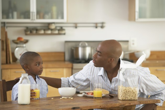 Father and son (5-7) looking at each other at breakfast table