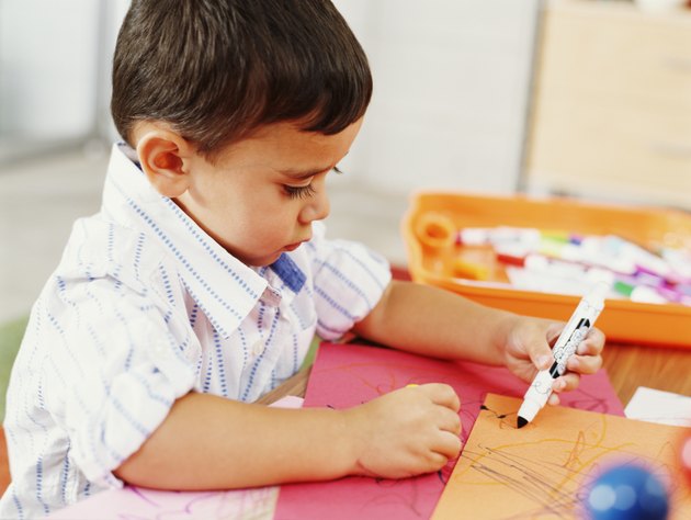 Boy (3-5 years) at table scribbling with felt tip pen, close-up, side view