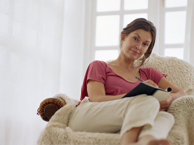 Woman relaxing in armchair, holding pen and notebook, portrait