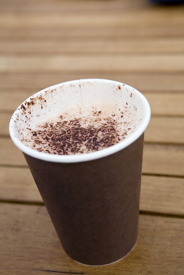 Cappuccino coffee in disposable cup on wooden table, close-up