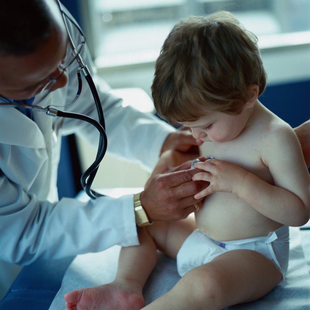 Doctor holding stethoscope to toddler boy's (18-21 months) chest