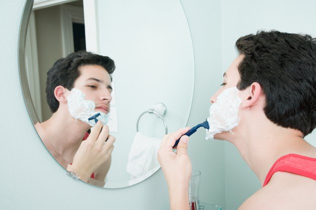 Boy shaving in mirror in bathroom