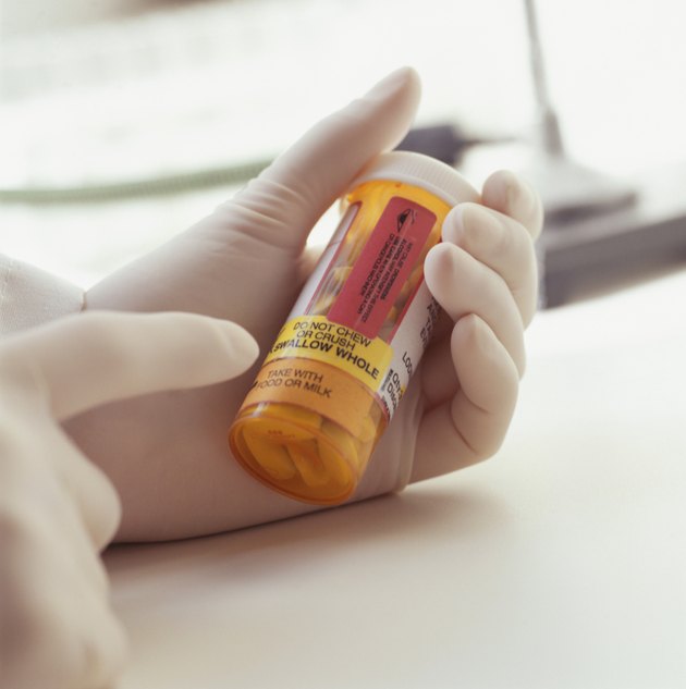 Person holding vial of pills, pointing at label, Close-up of hands