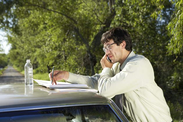 Businessman leaning on car, using cell phone, side view, close-up