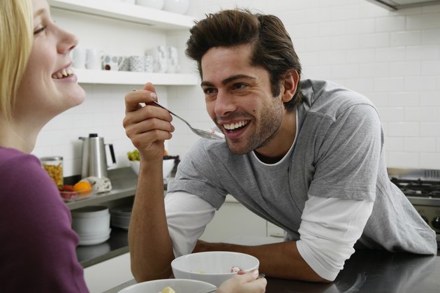 Couple in kitchen, man holding spoonful of food, laughing