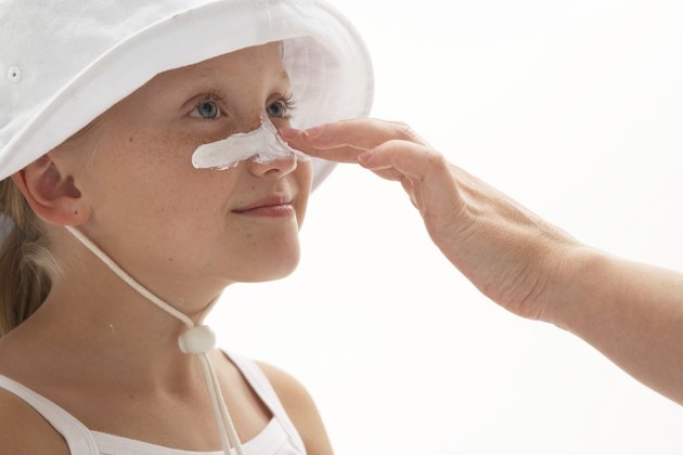 Girl (7-9) having sun cream applied to nose