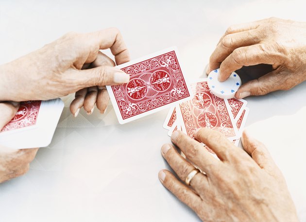 Close-Up on the Hands of a Senior Man and Woman Holding Playing Cards and Gambling Chips