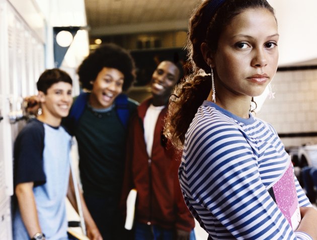 Serious Female Student Looking at the Camera, with Three Boys Standing in the Background Laughing at Her