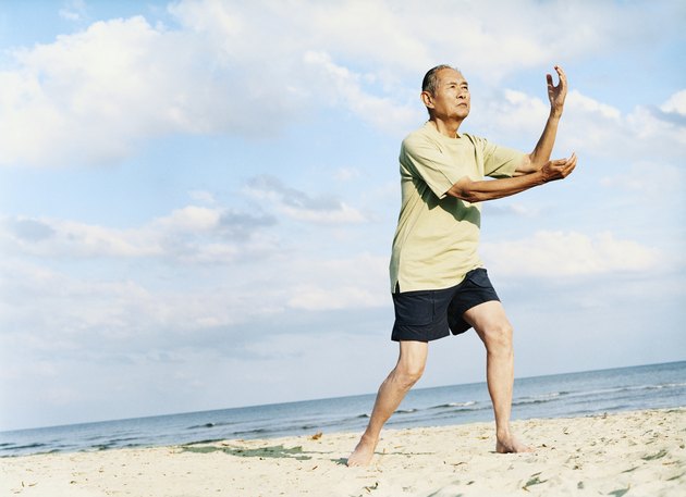 Senior Man Stands on the Beach Doing Tai Chi