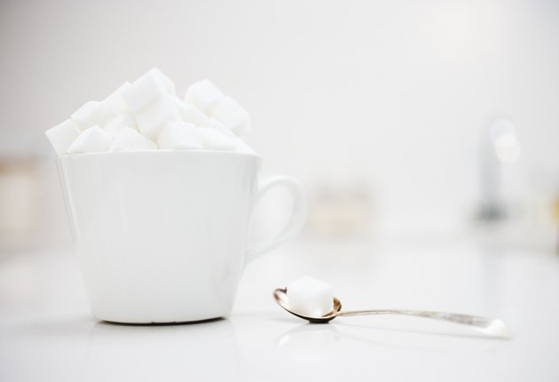 Sugar cubes filling coffee cup next to spoon with sugar cube