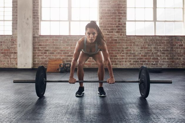 Female performing deadlift exercise with weight bar. Confident young woman doing weight lifting workout at gym.