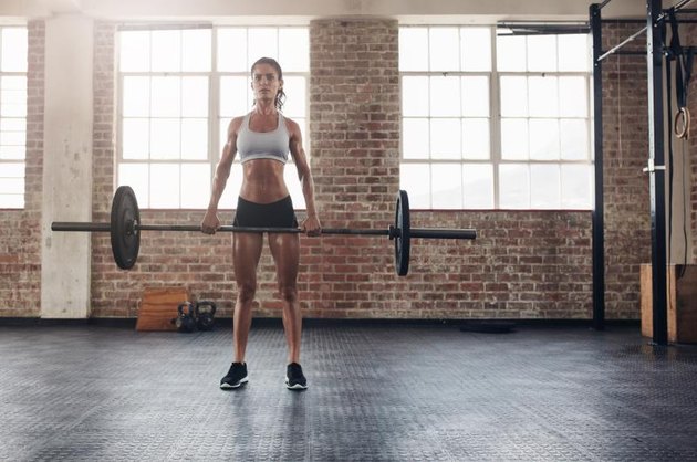 Full length portrait of muscular woman in a gym doing heavy weight exercises. Fitness female doing weight lifting at health club.