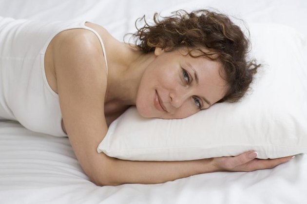 Mid adult woman lies on pillow smiling at camera