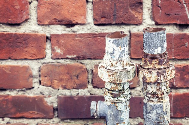 Old rusty cut pipes on a brick wall background.