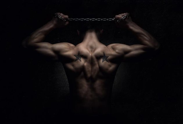 Rear view of muscular sports man stretching out over dark concrete background