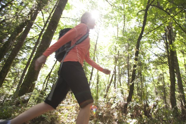 Woman hiking up hill in forest in sunlight