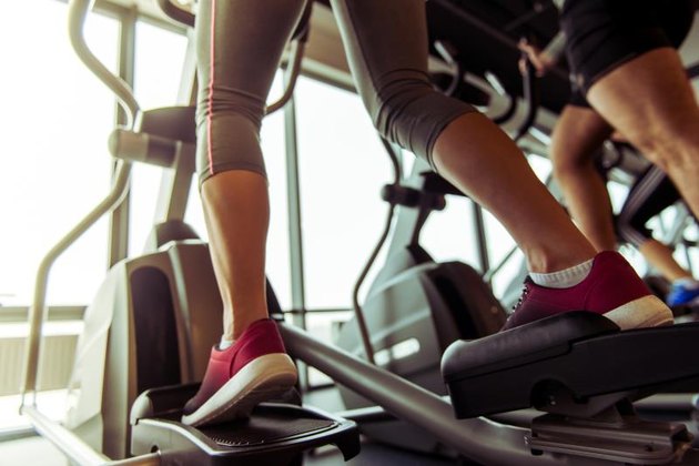 Back view of attractive young people working out on an elliptical trainer in gym