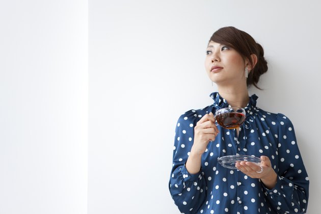Young woman leaning on wall and looking away, holding cup of tea, white background, copy space
