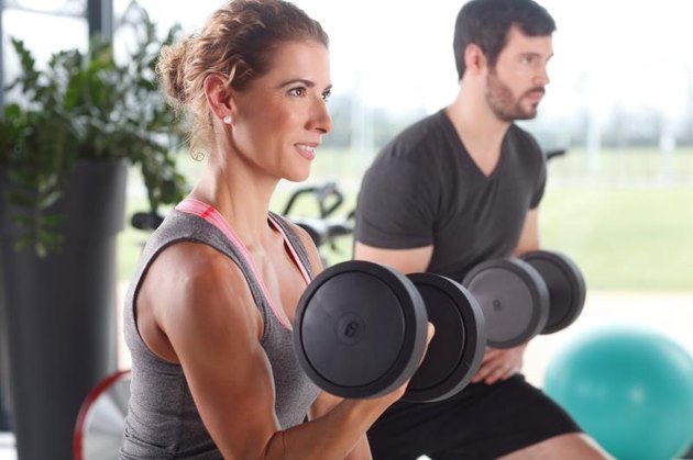 Portrait of woman and man lifting barbells during a gym workout at fitness center.