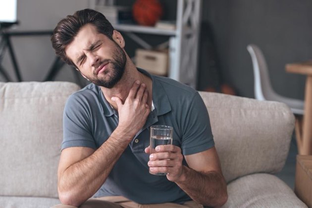 Frustrated young man touches his neck while holding a glass of water