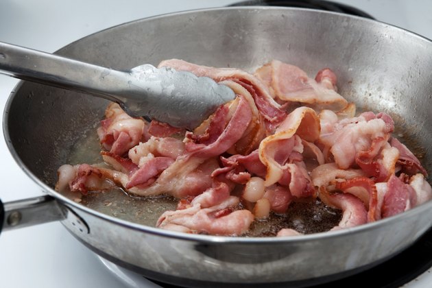 Sizzling bacon in a pan on the stove being stirred