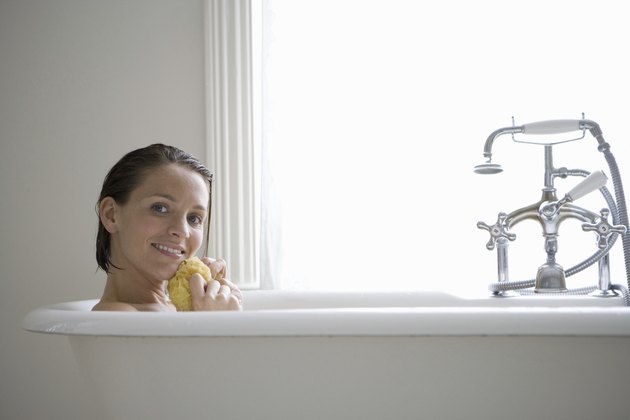 Young woman with sponge in bath, smiling, portrait