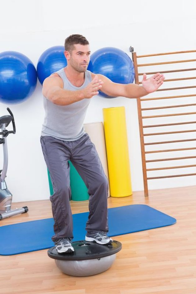 Concentrate man training in bosu ball in fitness studio