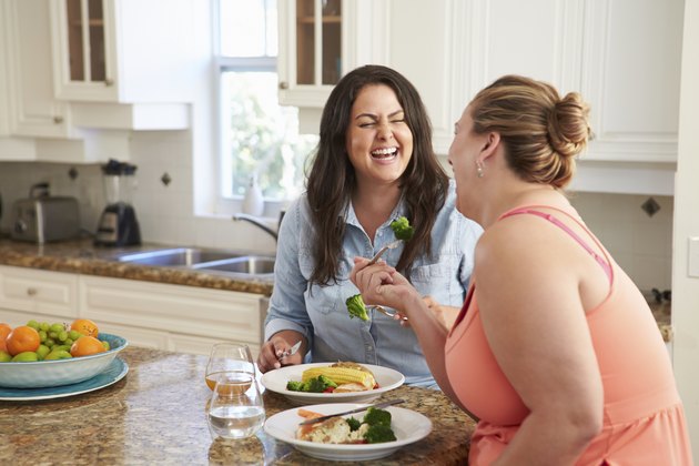 Two Overweight Women On Diet Eating Healthy Meal In Kitchen