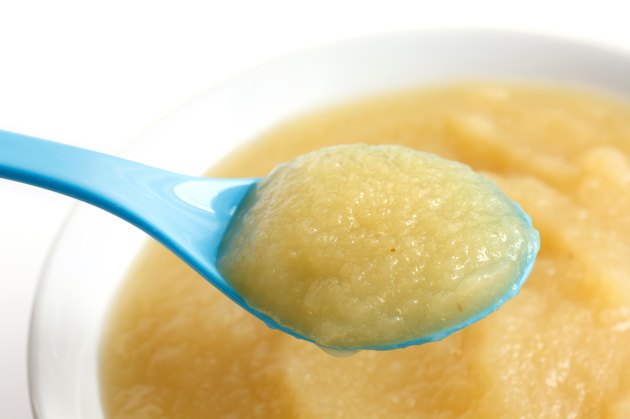 White dish of apple sauce with blue baby spoon.