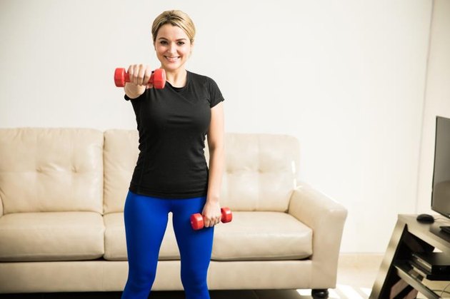 Pretty young Hispanic woman lifting weights and working out at home