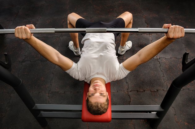 young man doing bench press workout in gym
