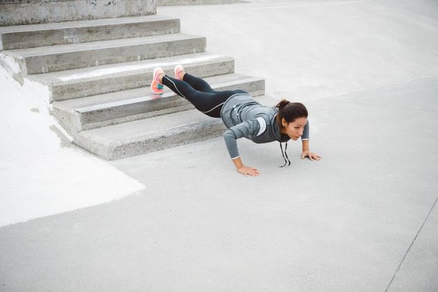 Urban fitness woman workout doing feet elevated push ups and exercising outdoor. Motivated female athlete training hard.