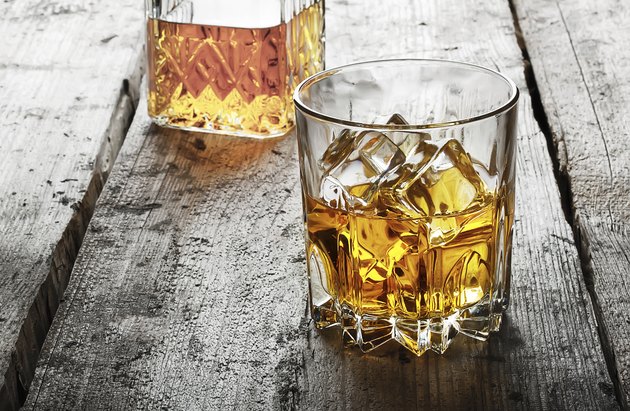 Faceted glass of whiskey with ice and a decanter