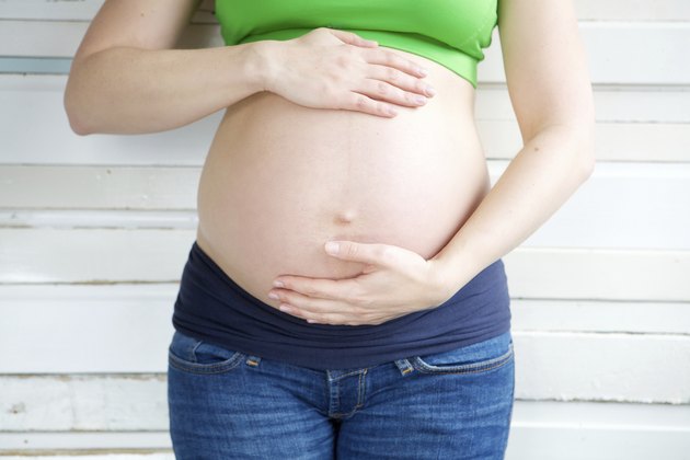 Young pregnant woman in jeans holding stomach